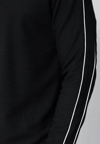 Chemise noire à manches longues avec des bandes latérales blanches, fabriquée en tissu côtelé. Le design est conçu pour être ajusté avec un col rond et une texture lisse.