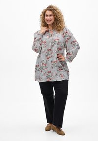 Tunique à motif floral en rayures blanches et bleues marine, avec des manches ballon et un col en keyhole, associée à un pantalon noir et des chaussures beiges.