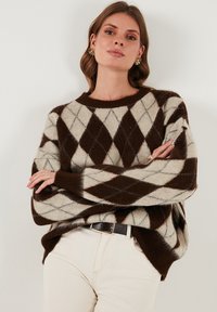 Rjav in krem svetrovni pulover z argyle vzorcem, ki ima dolge rokave, okroglo ovratnico ter sproščen kroj z rebrastimi manšetami.