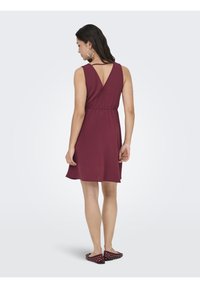 Robe sans manches bourgogne avec un dos en V, taille élastique et jupe évasée, assortie à des ballerines noires à pois blancs.