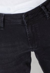 Pantalones de mezclilla oscura con una textura suave, que presentan un cierre de botón, trabillas para el cinturón y detalles en los bolsillos delanteros.