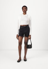 White knitted crop top with collar, black denim shorts with frayed hem, black flats, and small black bag with a logo detail.