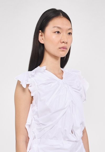Haut sans manches blanc en tissu léger, présentant des détails froncés, des accents de manches à volants et un design central torsadé.