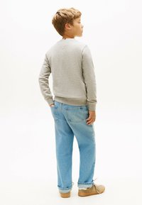 Szary sweter z okrągłym dekoltem, zestawiony z jasnoniebieskimi, luźnymi dżinsami. Brązowe buty z widocznymi sznurówkami w okolicy kostek.