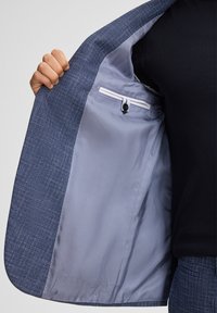 Blazer blu navy con una superficie texturizzata e fodera azzurro chiaro liscia. Presenta una tasca interna con chiusura a bottone e un dettaglio a righe a contrasto.