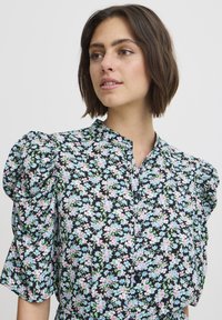 Bluză florală cu un fundal negru, flori în nuanțe pastel de roz și albastru, mâneci scurte pufoase și un guler înalt cu închidere cu nasturi.