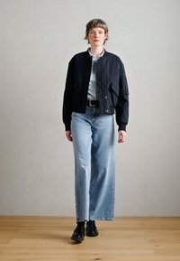 Mustast bomberjopest, millel on ees tõmblukk, kantud hele sinise särgi peal. Laia säärega helesinised teksapüksid ja mustad saapad. Siledad tekstuurid.