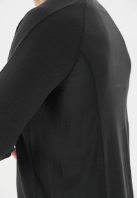 Schwarz sportliches Shirt mit glatter Textur und Netzpaneelen. Das Design umfasst lange Ärmel und eine taillierte Passform.