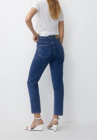 Blue high-waisted jeans with a straight-leg fit, featuring back pockets and frayed hems, paired with white wedge sandals and a white t-shirt.