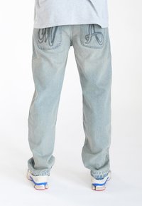Jeans de mezclilla de lavado claro con un corte holgado. Presentan grandes bolsillos traseros bordados y una textura ligeramente desgastada. Diseño estándar de cinco bolsillos.