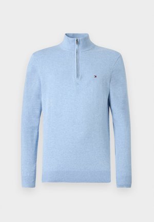 Vaaleansininen pitkähihainen neule, jossa on neljänneksen vetoketjulla varustettu kaulus ja pieni punainen, valkoinen ja sininen logo rinnassa.