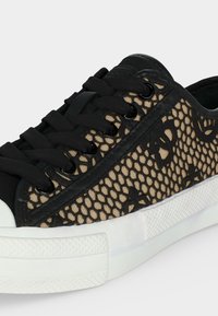 Gros plan d’une basket noire et beige avec une tige en mesh à motifs, des lacets noirs et une semelle extérieure en caoutchouc blanche texturée.
