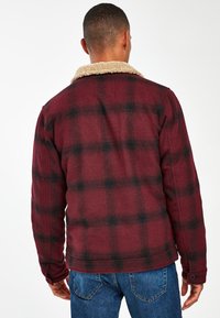 Rood en zwart geblokt jack met een beige, schapenvacht kraag. Heeft knoopmanchetten en een gestructureerde stof in een relaxed fit.