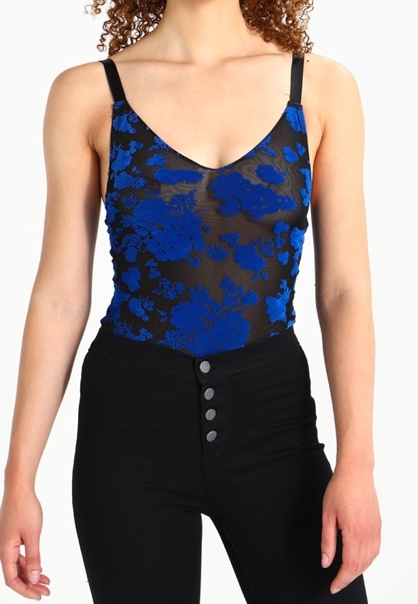 Czarny siateczkowy kombinezon z niebieską haftowaną kwiatową aplikacją, głębokim dekoltem w serek i cienkimi, regulowanymi ramiączkami, zestawiony z czarnymi spodniami z wysokim stanem.