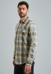 Chemise en plaid, boutonnière, beige, bleue et noire. Dotée d'une poche poitrine, de manches longues et d'un col pointu. Matériau en coton, texture douce.