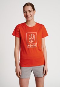 Rode katoenen t-shirt met een wit geometrisch grafisch ontwerp en de tekst "GGI2." Het shirt heeft korte mouwen en een ronde hals.