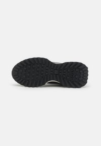 Fekete gumi sneaker talp, texturált járófelülettel, kiemelkedő geometriai formákkal és szürke akcentussal a sarkán.