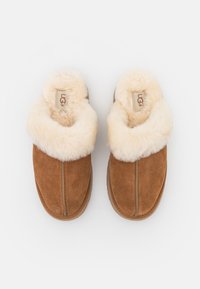 Chaussons à enfiler en daim marron avec doublure épaisse en polaire crème et marque UGG visible à l'intérieur.