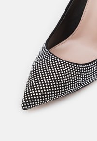 Escarpin noir en daim à talons hauts, orné de pierres à rhinestones argentées, avec un bout pointu et une doublure intérieure lisse.