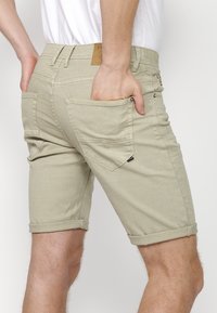 Bermudas color caqui claro hechas de una mezcla de algodón. Presentan dobladillos enrollados, bolsillos traseros con solapa y una etiqueta de cuero en la cintura.
