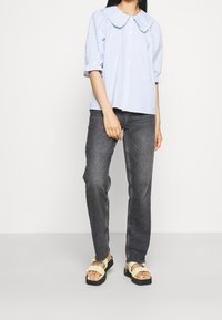 Chemise rayée bleu clair et blanche avec un grand col, manches courtes bouffantes, bouton devant, associée à un jean gris foncé et des sandales à plateforme beiges.