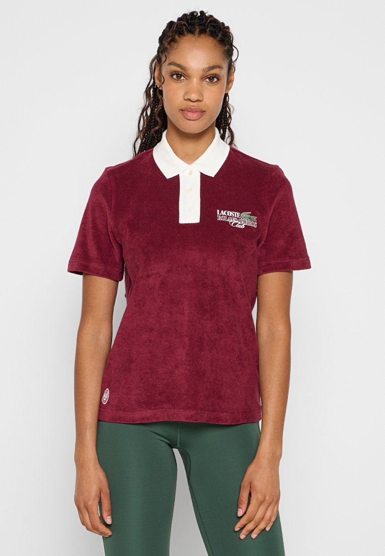 Polo bourgogne en doux tissu éponge avec un col blanc et des détails de logo brodés sur la poitrine. Manches courtes et coupe décontractée.