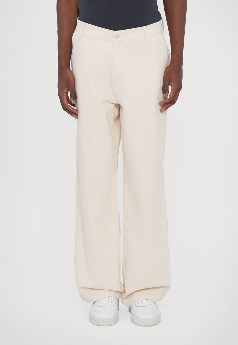 Wide-leg trousers in a soft cream fabric, featuring a classic button closure and side pockets, paired with white sneakers.