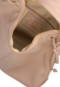 Licht beige leren handtas met een textuur, gouden rits en een label aan de binnenkant. Ronde vorm met geknoopte accenten aan de zijkant.