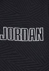 Tissu noir texturé avec des lettres blanches brodées formant le mot "JORDAN" en style gras et bloc.