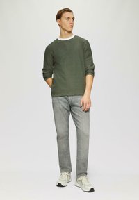 Chemise à manches longues verde olive avec col rond, associée à un jean gris clair et des baskets claires. Design simple et décontracté avec une coupe ample.