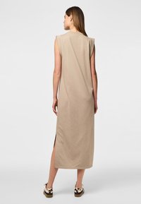 Vestido midi sin mangas color crema, con aberturas laterales, hecho de una tela suave. Diseño sencillo con cuello redondo y corte holgado.