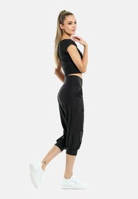 Sort cropped top og sorte joggerbukser med afsluttede ankler; materialet ser glat og strækbart ud; har lommer og en afslappet pasform.