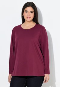 Bordeaux lange mouwen shirt van zachte stof met een ronde hals en een ontspannen pasvorm, gecombineerd met donkere jeans. Eenvoudig ontwerp zonder zichtbare patronen.