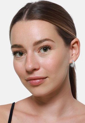 Zilveren hoepel oorbellen met een gestructureerd oppervlak, die een gladde, ronde vorm laten zien. De teint van het model is licht, met een natuurlijke make-up.