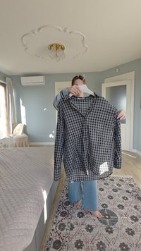 Črno-bela karo srajca na gumbke iz lahkega tkanega materiala, z ovratnikom in dolgimi rokavi, obešena na obešalniku.