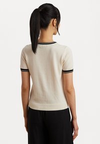 Svetlobežový sveter s krátkymi rukávmi a čiernymi pruhovanými akcentmi na golieri a rukávoch, s priliehavým strihom a hladkou textúrou.
