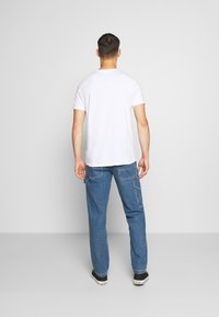 Valkoinen lyhythihainen t-paita, jonka kanssa on väljät siniset farkut, joissa on taskut ja rento istuvuus. Yksinkertainen muotoilu ilman näkyviä kuvioita.