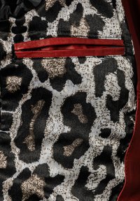 Musterstoff mit einem schwarz-braunen Leopardenmuster, einem roten Akzentstreifen und einer kleinen strukturierten Tasche. Weiche, glatte Textur.
