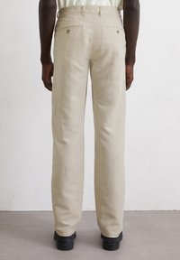 Light beige linen pants with a straight leg design, featuring two back pockets and classic button detail, paired with black footwear.