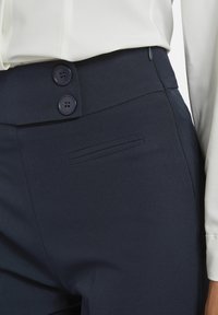 Marineblauwe op maat gemaakte pantalons hebben twee knopen in de taille, een strakke textuur en een discreet geplaatste zijzak voor functionaliteit.