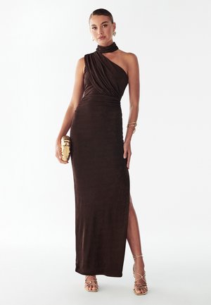Robe de soirée marron à une épaule avec texture drapée, fente latérale et silhouette ajustée. Pochette dorée avec un motif texturé tenue à la main.