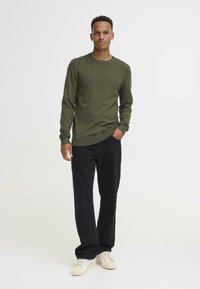 Oliven grønn strikkegenser med rund hals, kombinert med svarte bukser og krystallhvite joggesko. Teksturen er glatt med ribbede detaljer.