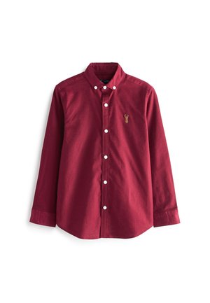 Chemise bordeaux à manches longues avec des boutons blancs et un petit emblème brodé d'un cerf doré sur le côté gauche de la poitrine.