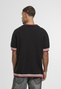 Polo de punto negro de manga corta con acentos en rojo y blanco a rayas en el cuello y las mangas, acabado texturizado y corte relajado.