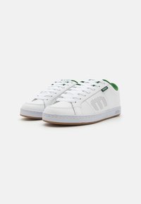 Sapatilhas brancas em couro com detalhes em verde, com perfurações e atacadores brancos. Apresentam uma sola de borracha com um piso castanho claro.