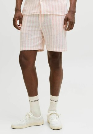 Mann iført hvite joggesko, hvite ankelsokker med svart tekst, og lyse shorts med vertikalt stripet mønster.