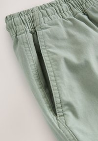 Shorts verts en coton avec une ceinture élastique, dotés de poches latérales et d'une texture lisse. Les coutures sont soigneusement réalisées.