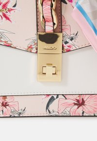 Handtasche mit floralem Muster in Pink, goldenen Akzenten und einem glatten weißen Grund. Sie verfügt über einen goldenen Verschluss und Akzente mit einem dekorativen Schal.