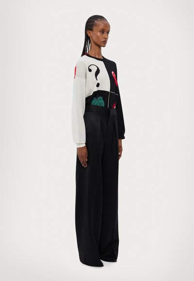 Sweater med et grafisk design i grå, sort og rød med spørgsmålstegn og bladmotiver. Kombineret med sorte bredbenede bukser.
