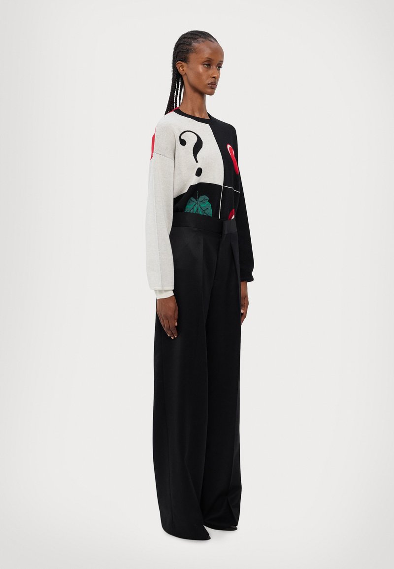 Maglione con un design grafico in grigio, nero e rosso, caratterizzato da motivi a punto interrogativo e foglia. Abbinato a pantaloni larghi neri.
